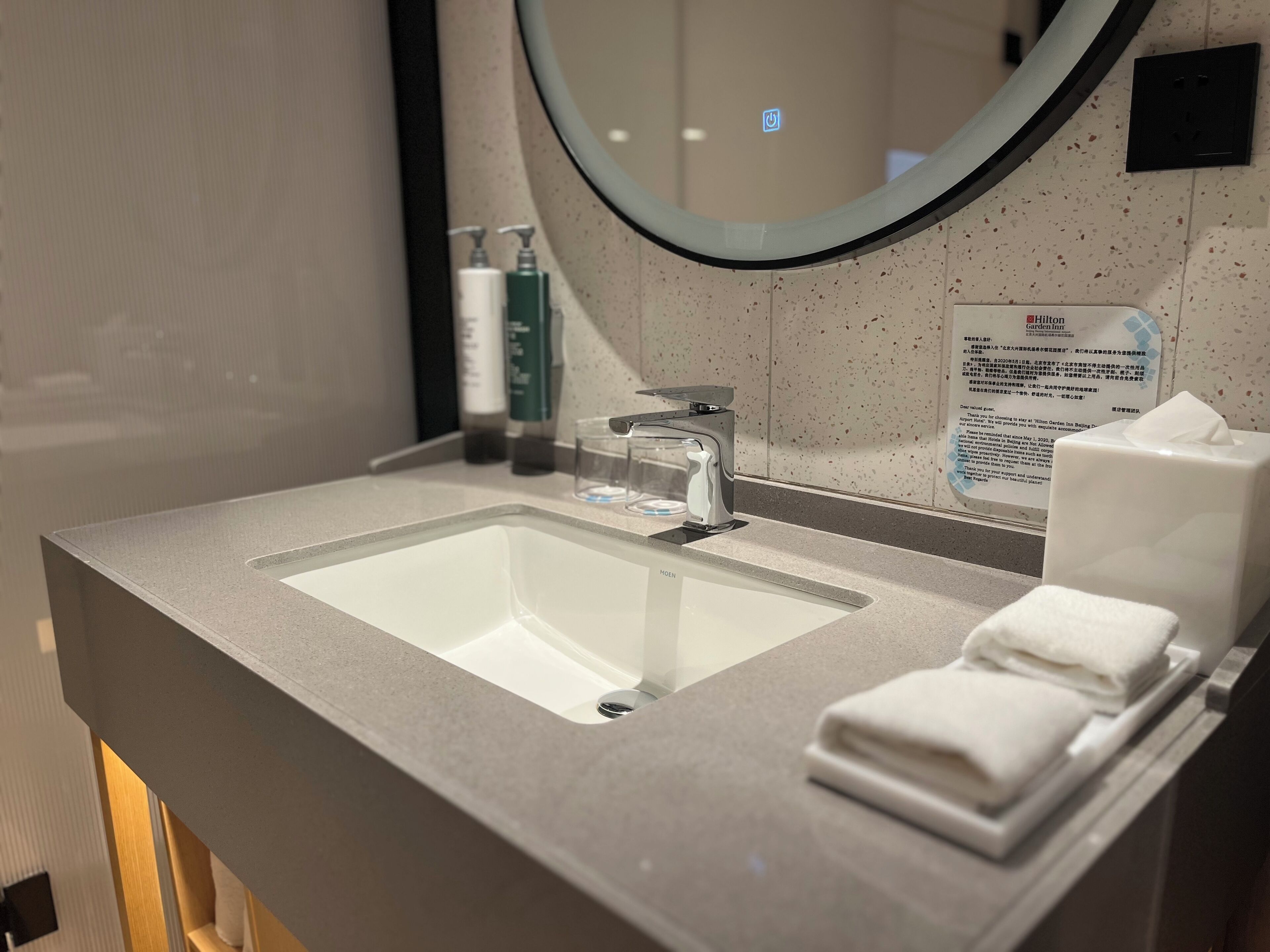 Un baño de hotel con un lavabo grande, un espejo y artículos de aseo en la encimera.