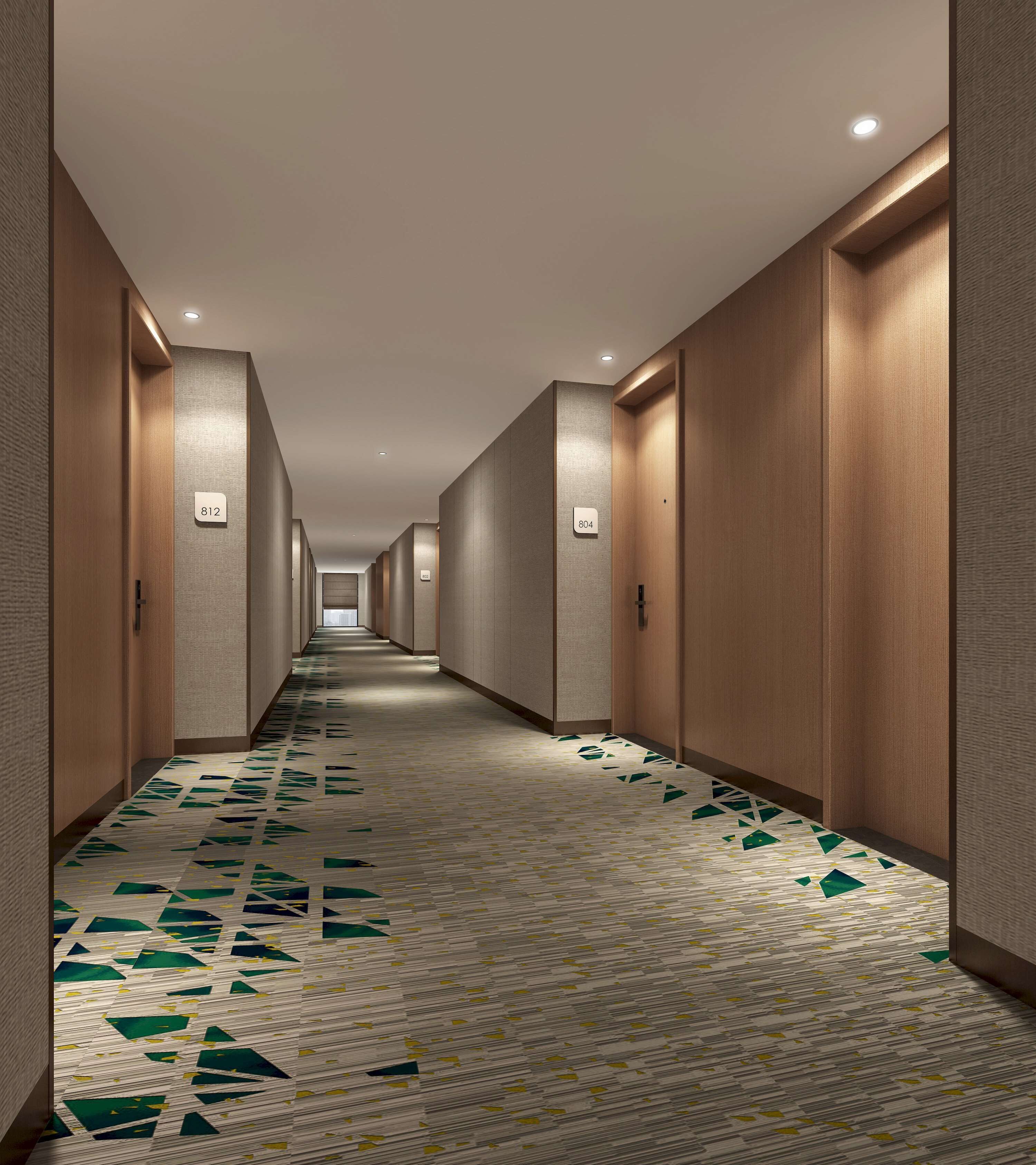 A long, narrow hotel corridor with numbered doors, recessed lighting, and patterned carpet.