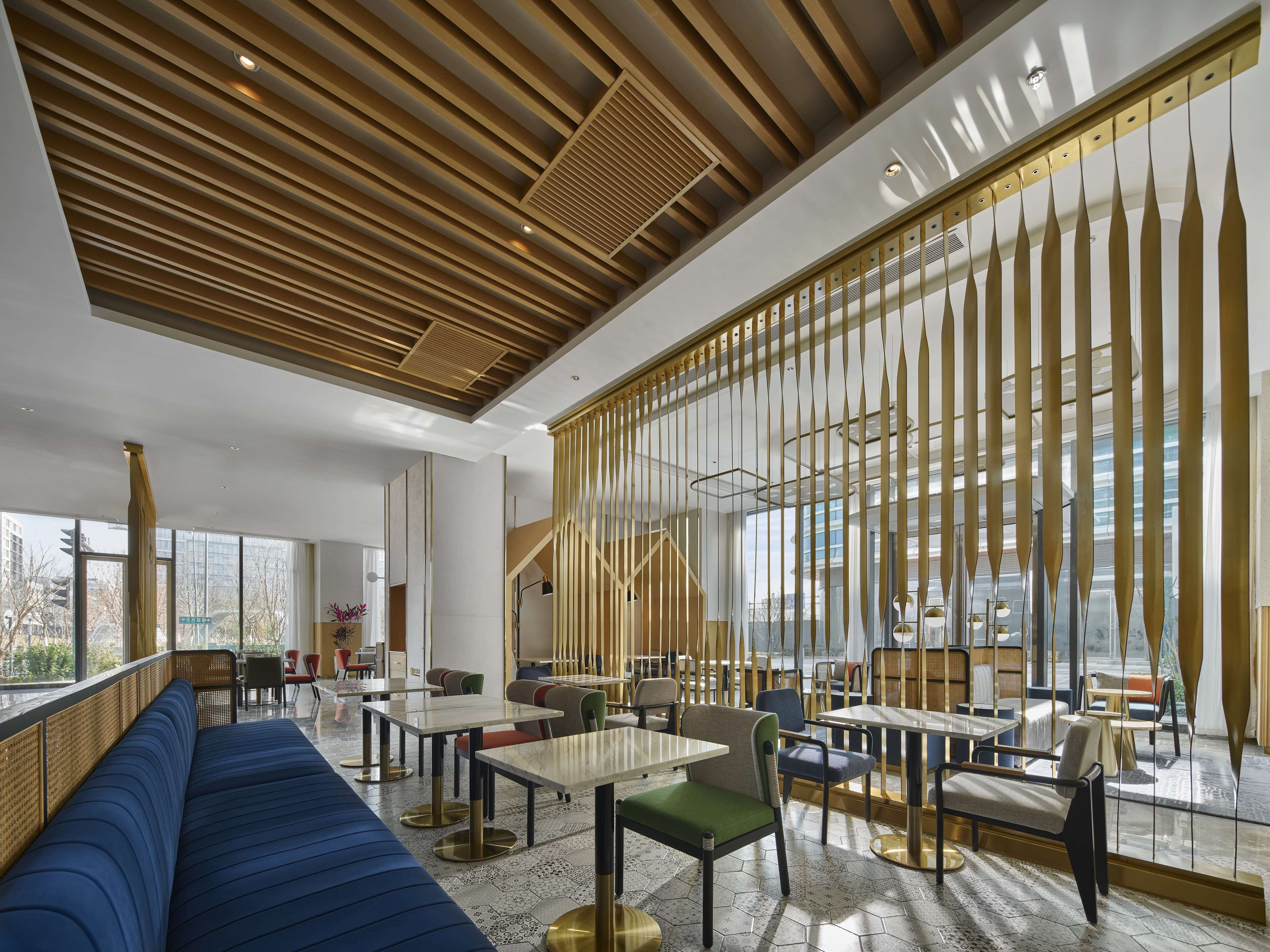 Un interior moderno con un sofá azul largo, mesas, sillas y un techo decorativo de madera.