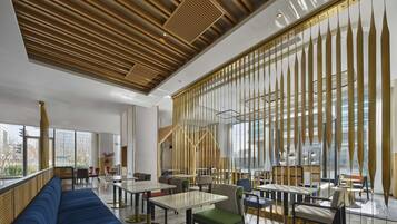 Un interior moderno con un sofá azul largo, mesas, sillas y un techo decorativo de madera.