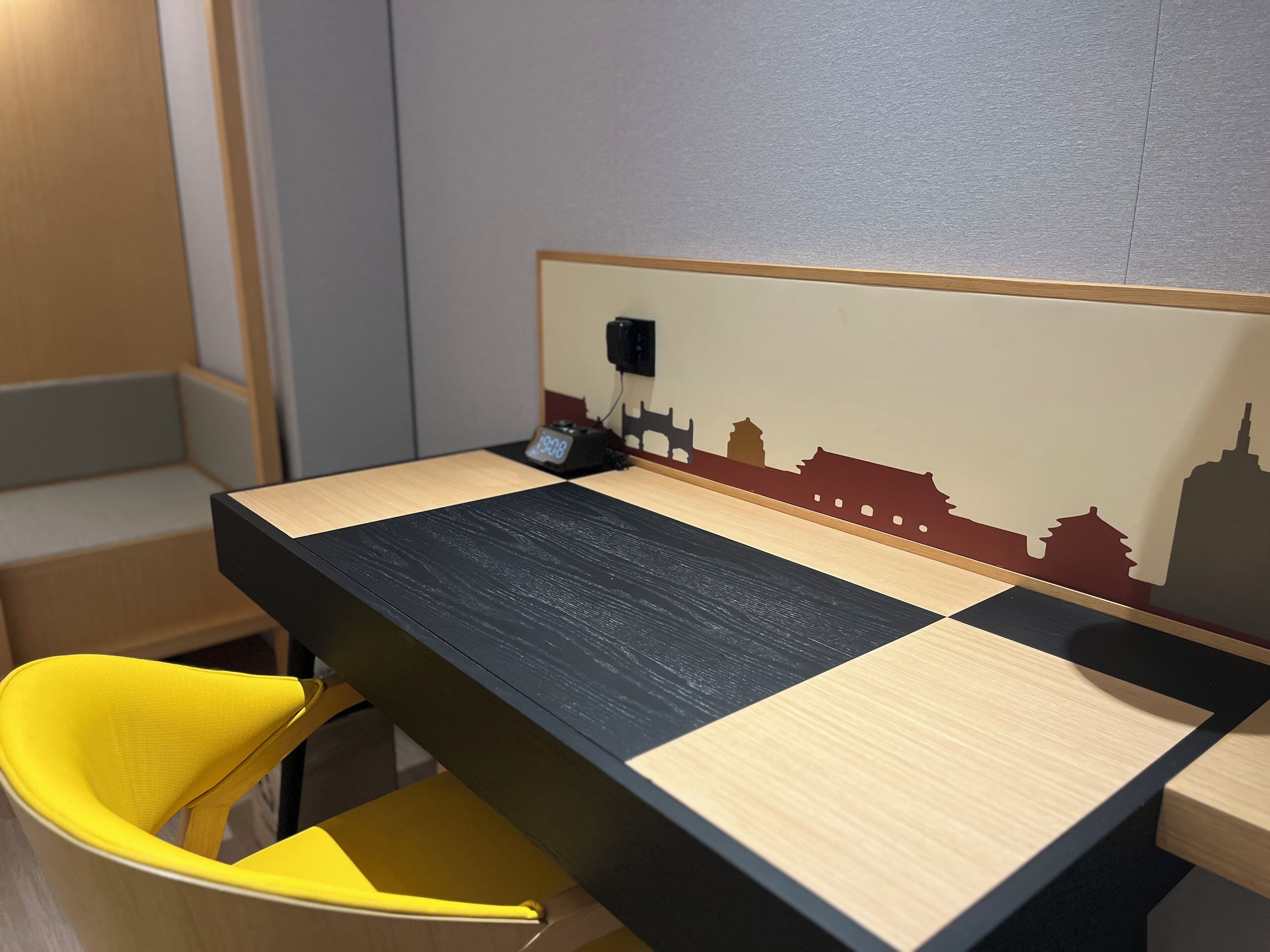 Una habitación con cama, una mesita de noche, una silla y un muro con silueta del horizonte.