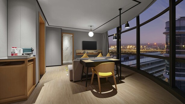 A modern hotel room with a dining area, a TV, and a city view.