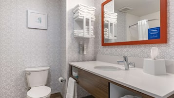 A modern bathroom with a toilet, sink, and mirror. There are towels and toiletries visible.