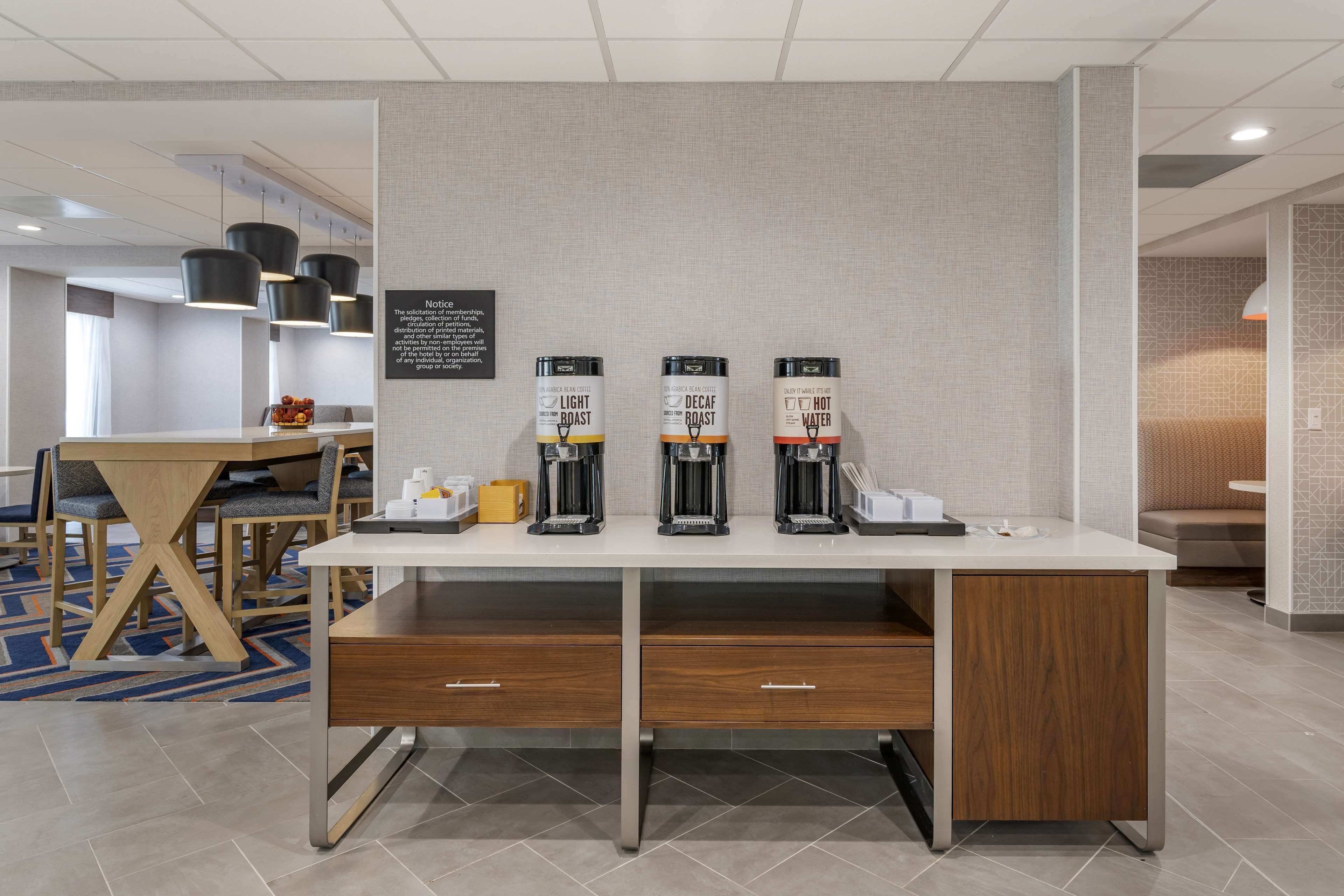 A hotel room with a white desk, three coffee machines, and a small table with chairs.