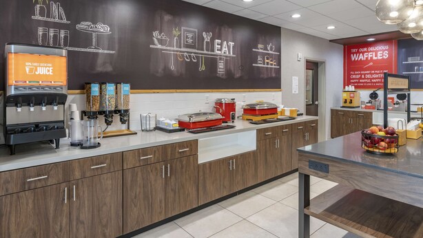 A modern kitchen area with a juice station, a waffle display, and a counter with various kitchen appliances. - Hampton Inn Nicholasville Brannon Crossing (Nicholasville)