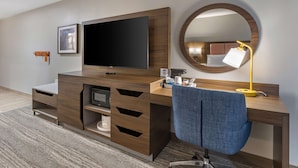 A modern hotel room with a wooden desk, a flat-screen TV, a round mirror, and a blue chair. - Hampton Inn Nicholasville Brannon Crossing (Nicholasville)