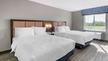 Quarto de hotel com duas camas, uma janela grande com vista, mesa de cabeceira com abajur e piso carpeteado.