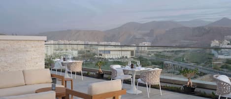 A rooftop terrace with outdoor seating, a view of a cityscape and mountains.