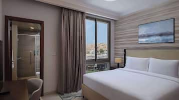 A hotel room with a large bed, a desk, a chair, a window with curtains, and a painting on the wall.