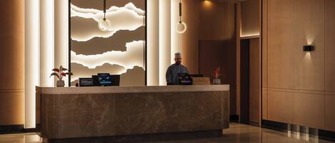 Un área de recepción de hotel moderna con un mostrador de mármol, una pantalla digital y una pared decorativa con motivos que recuerdan a nubes.