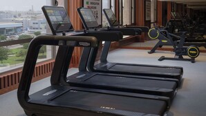 A gym with treadmills and exercise equipment, large windows with a city view, and a motivational poster on the wall.