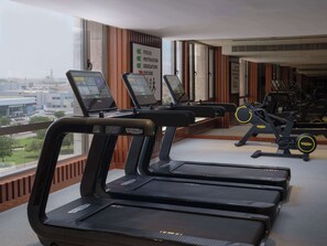 A gym with treadmills and exercise equipment, large windows with a city view, and a motivational poster on the wall.
