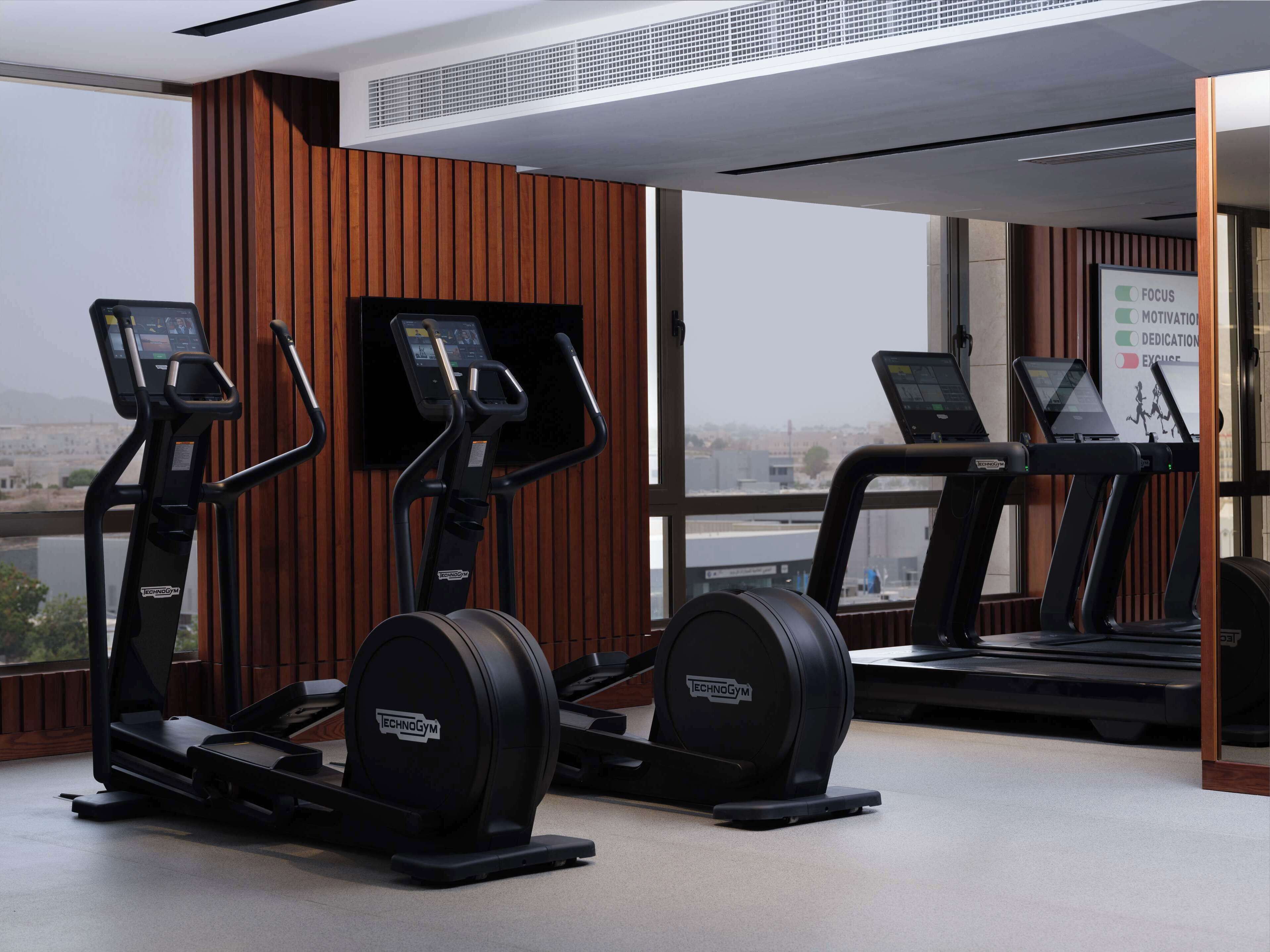 Un gimnasio con cintas de correr, elípticas y una máquina de remo.