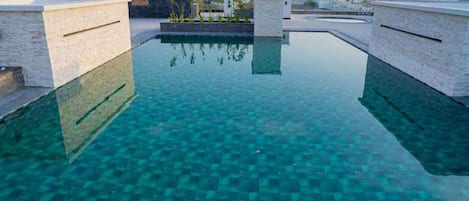 A rooftop infinity pool with clear blue water, surrounded by white walls and a mountainous backdrop.
