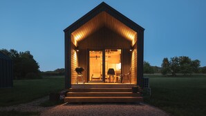 A wooden cabin with a porch, a grill, and a chair outside.