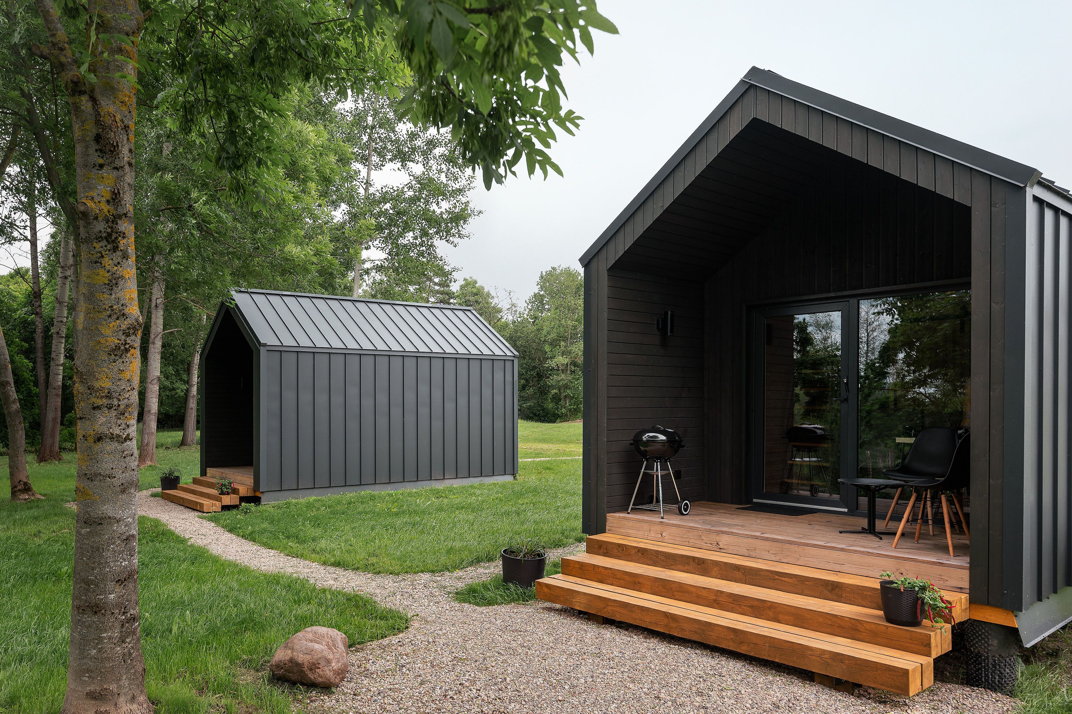 A modern cabin with a wooden deck, a small shed, and a grill area.
