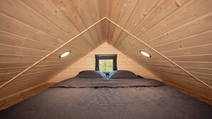 A bedroom with a sloped ceiling, a window, and a bed.