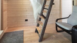 A person climbing a wooden ladder in a room with a wooden ceiling, a gray rug, and a black chair.