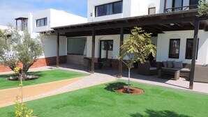 Un edificio moderno con un patio cubierto, mobiliario exterior y césped bien cuidado.