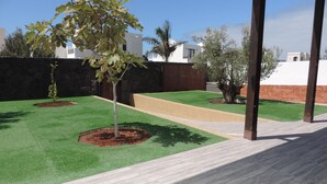 Un espacio al aire libre ajardinado con césped artificial, una terraza de madera y un muro de piedra.