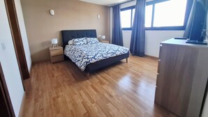 Un dormitorio con cama, mesitas de noche, un escritorio y un televisor.