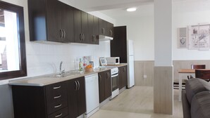 Una cocina moderna con armarios oscuros, lavavajillas, horno y microondas. Hay un comedor con mesa y sillas de madera.