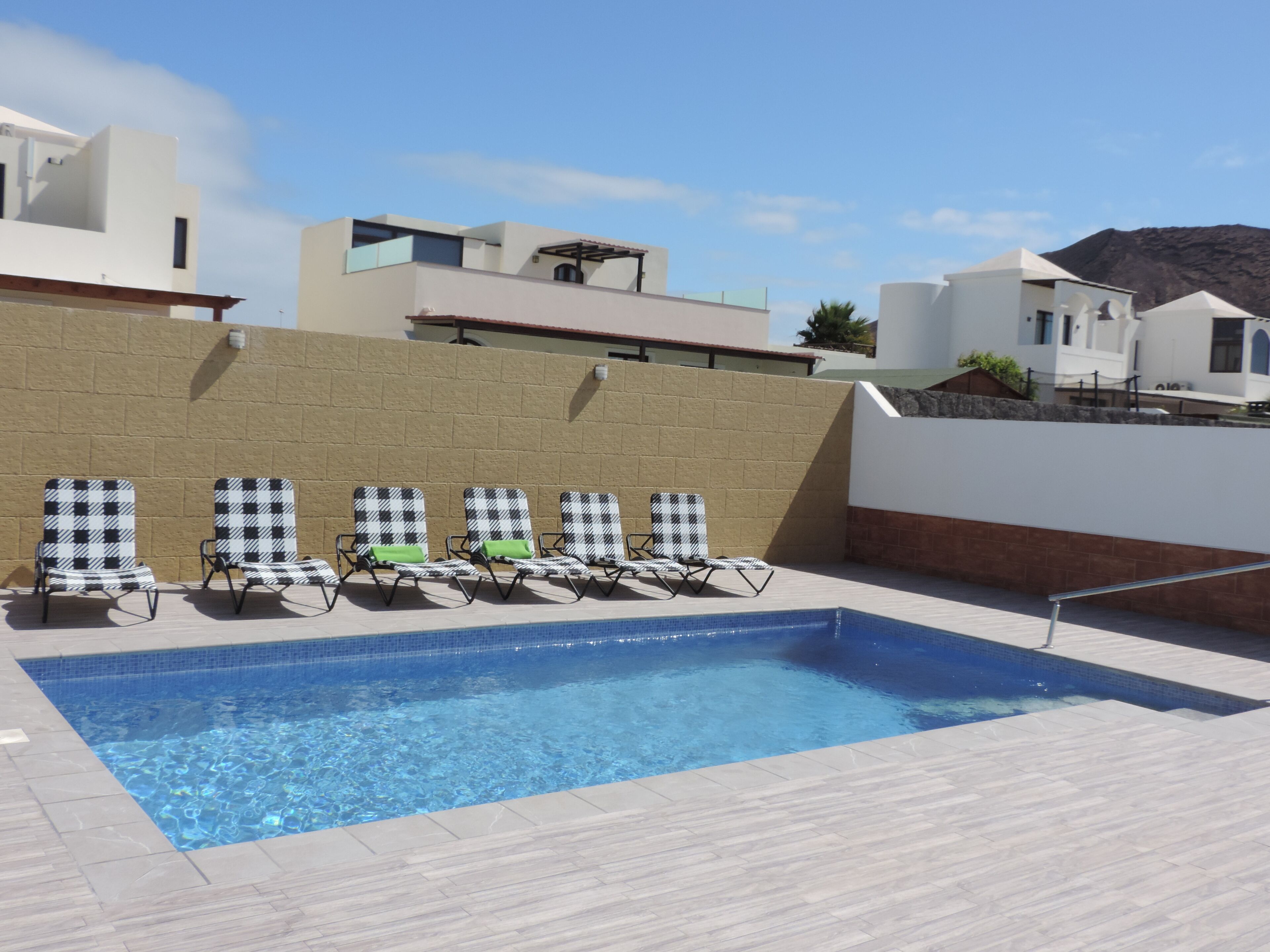 Une piscine entourée de chaises longues, un ciel bleu azur et des bâtiments modernes en arrière-plan.