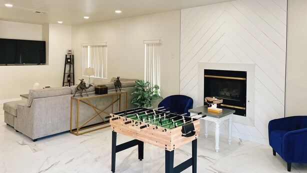A modern living room with a foosball table, a sofa, a television, and a fireplace.