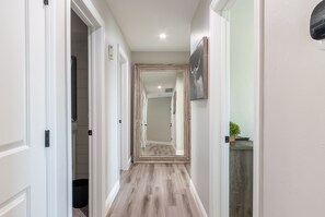 A hallway with wooden flooring, white walls, and a door leading to another room.