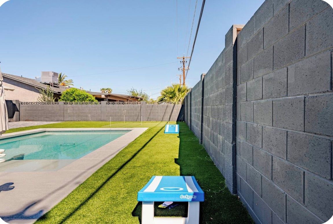 Une piscine entourée d’une pelouse et bordée d’un mur en briques.