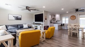 A modern living room with a sofa, yellow armchairs, a dining table, and a kitchen area with cabinets and a clock.