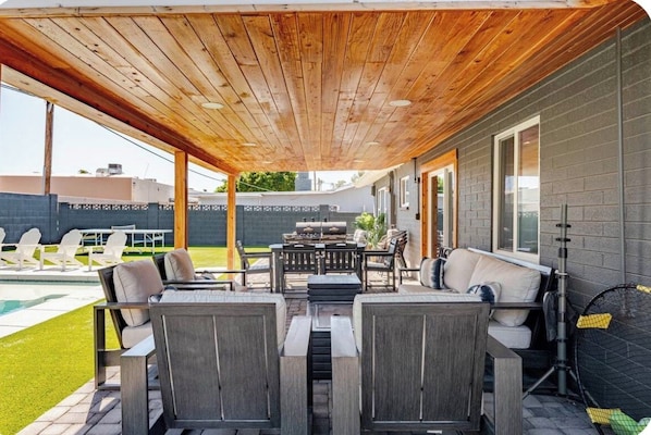 An outdoor patio with wooden ceiling, seating, and a pool.