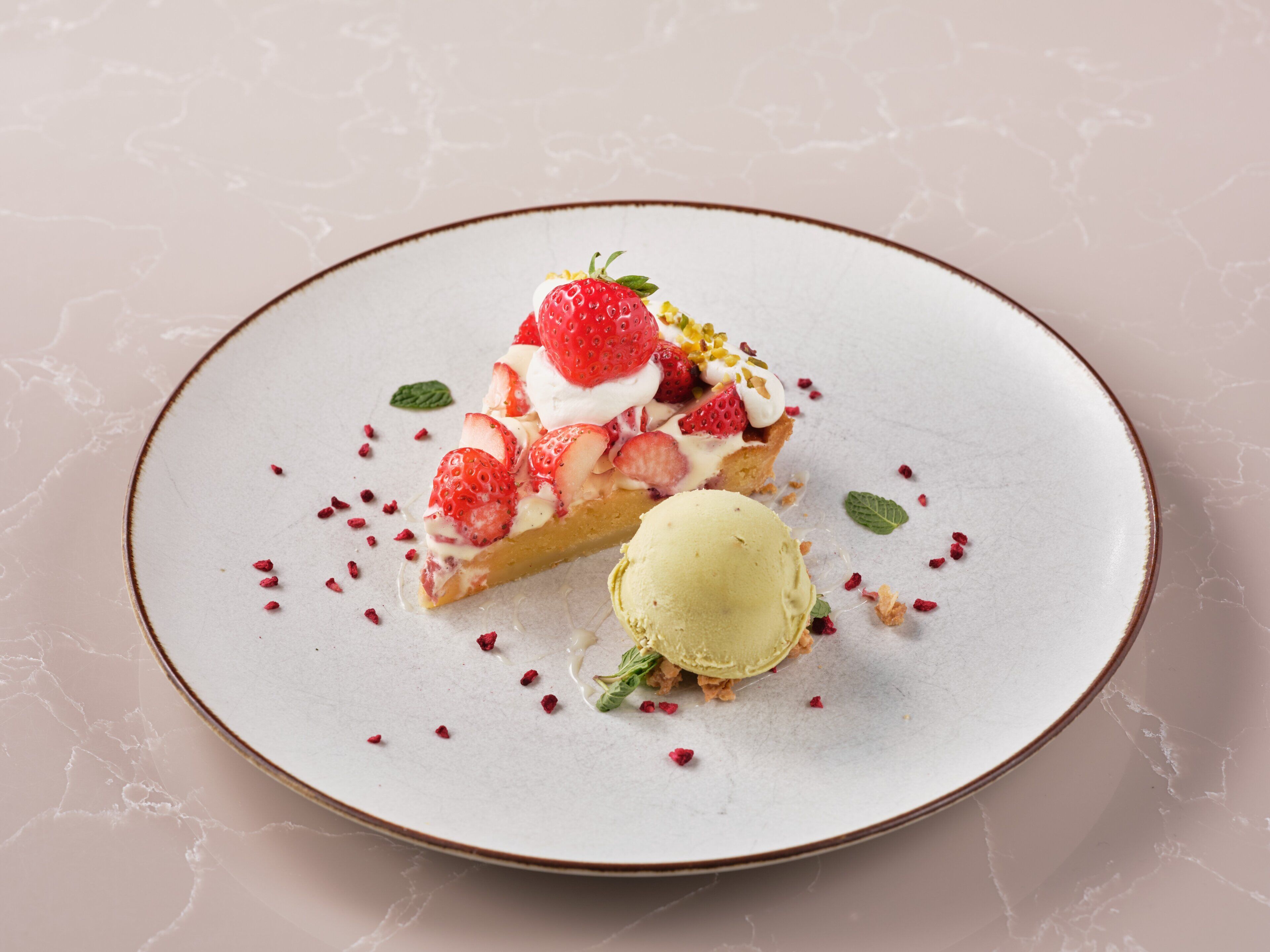 A dessert plate with a slice of cake topped with strawberries and whipped cream, accompanied by a scoop of ice cream.