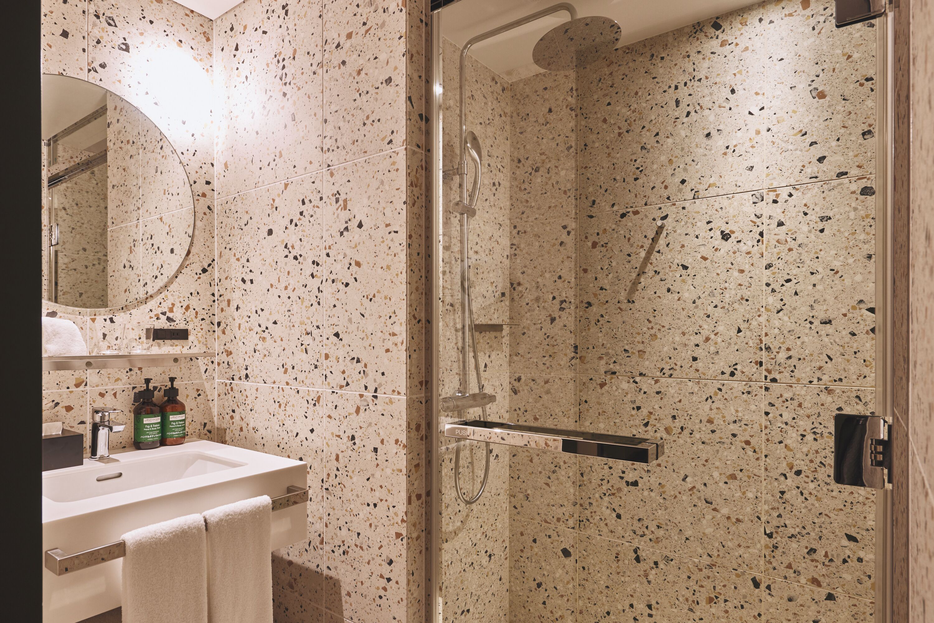 Un baño moderno con ducha envuelta en vidrio, un lavabo con espejo y artículos de aseo en la encimera.