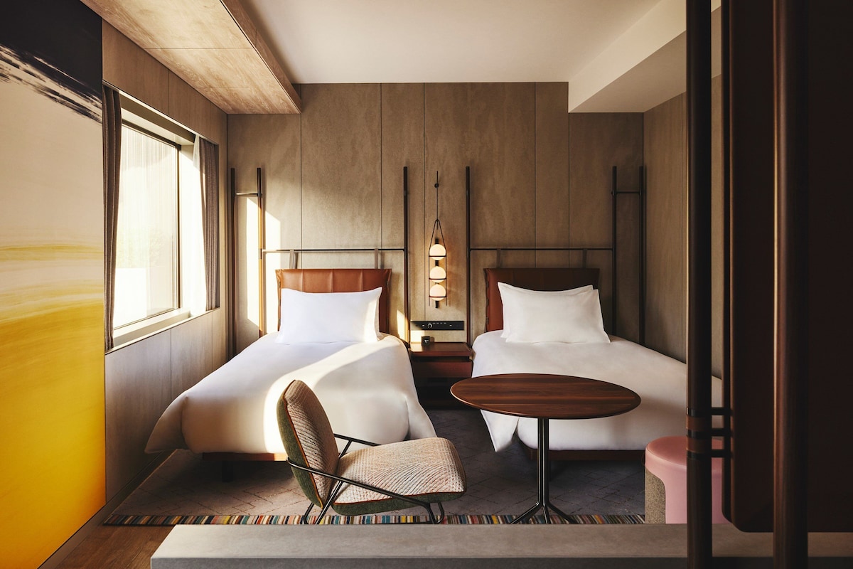 Una habitación de hotel con dos camas, una mesita, una silla y una mesita de noche.