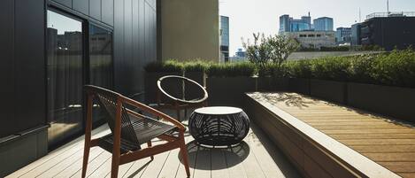 Terraza en la azotea con zona de estar, que incluye una silla y una mesa redonda, y vista del horizonte urbano al fondo.