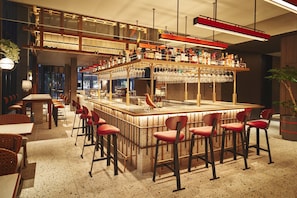 Zona de bar con diversas opciones de asientos, incluyendo taburetes de bar y mesas altas, así como una variedad de botellas y copas a la vista.