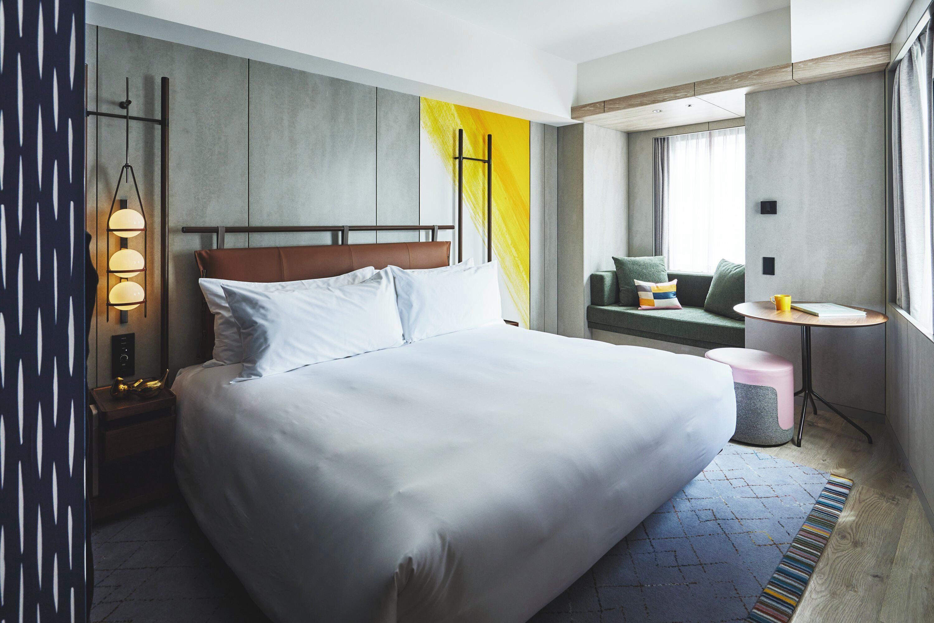 A modern hotel room with a large bed, a bedside table, a small round table, and a sofa.