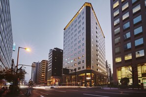 A modern hotel with a corner entrance, large windows, and a visible sign. - voco Osaka Central by IHG (Osaka)