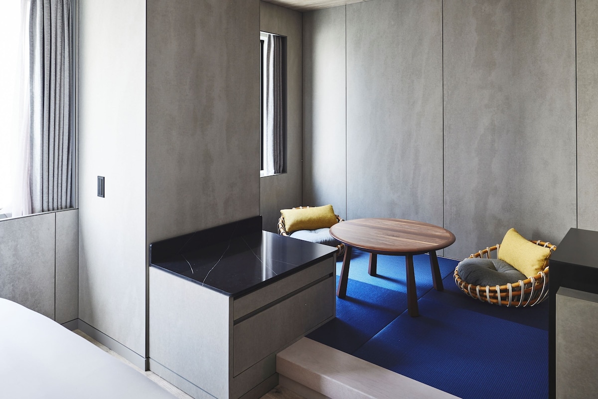 Una habitación moderna con una encimera negra, una mesa redonda de madera y una silla de mimbre con cojines.