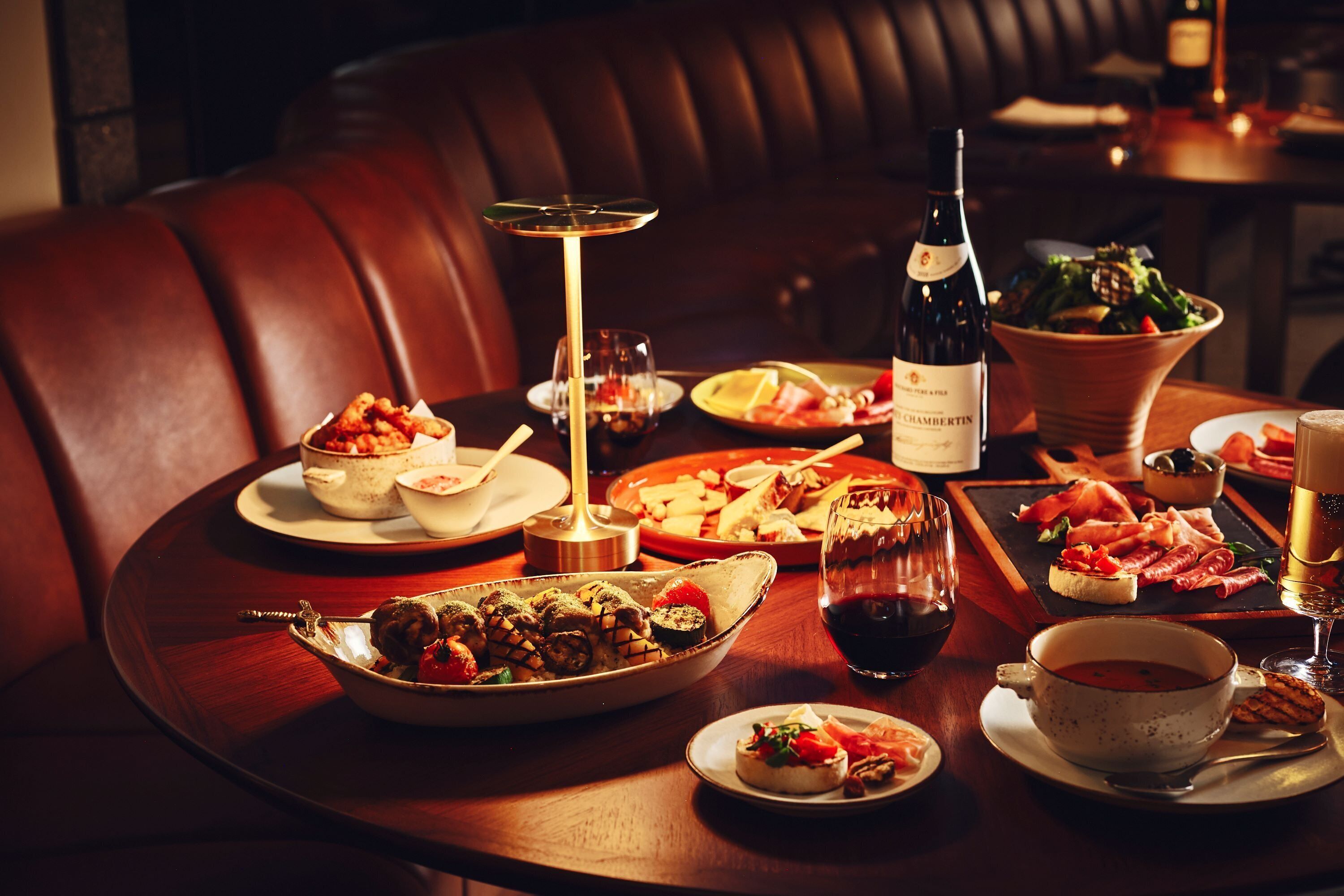 A dining table set with various dishes, a bottle of wine, and a glass of red wine.