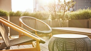 A wicker chair and a round table on an outdoor patio with a view of buildings and trees. - voco Osaka Central by IHG (Osaka)