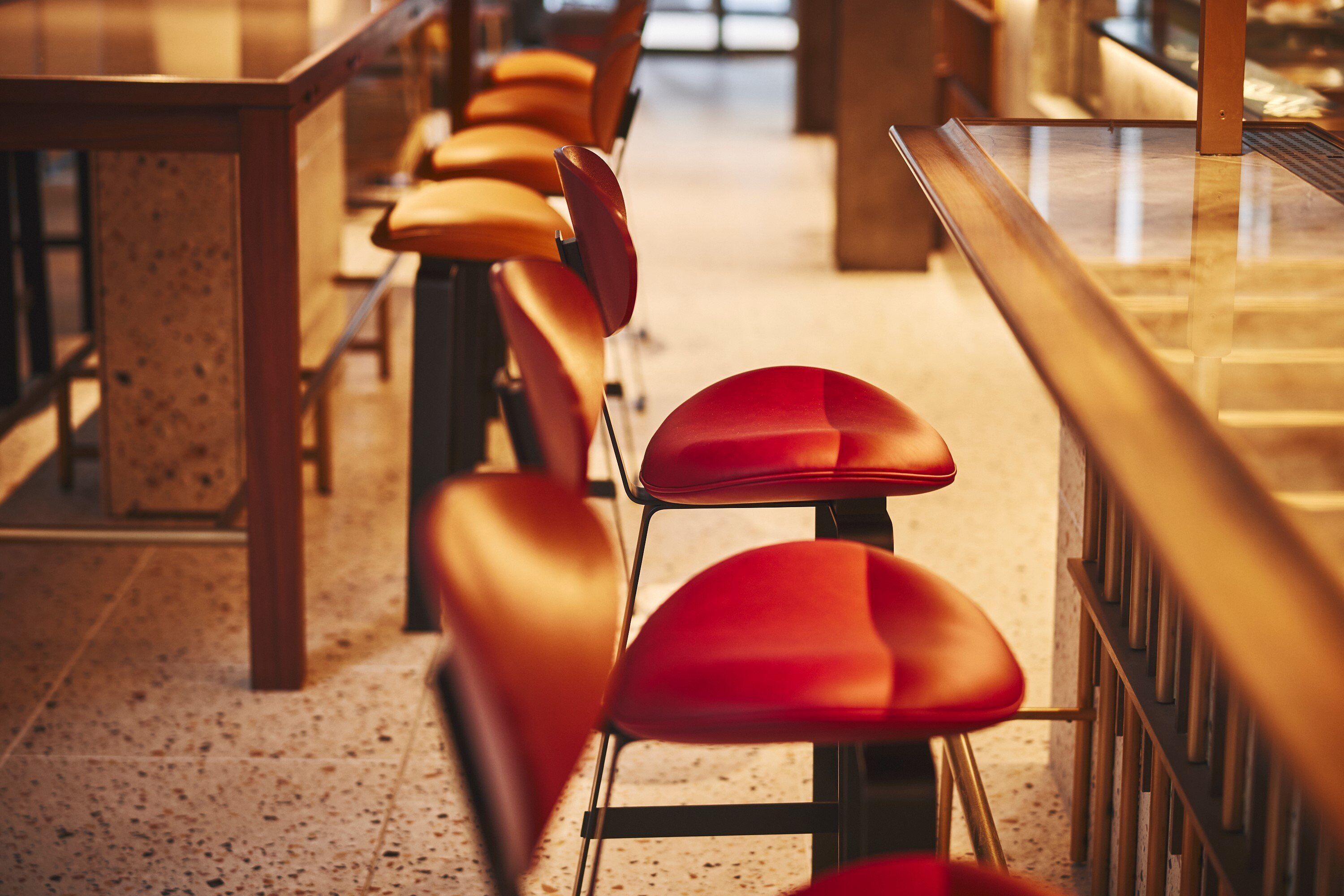 A row of red chairs with metal frames, arranged in a linear fashion along a corridor with a speckled floor.