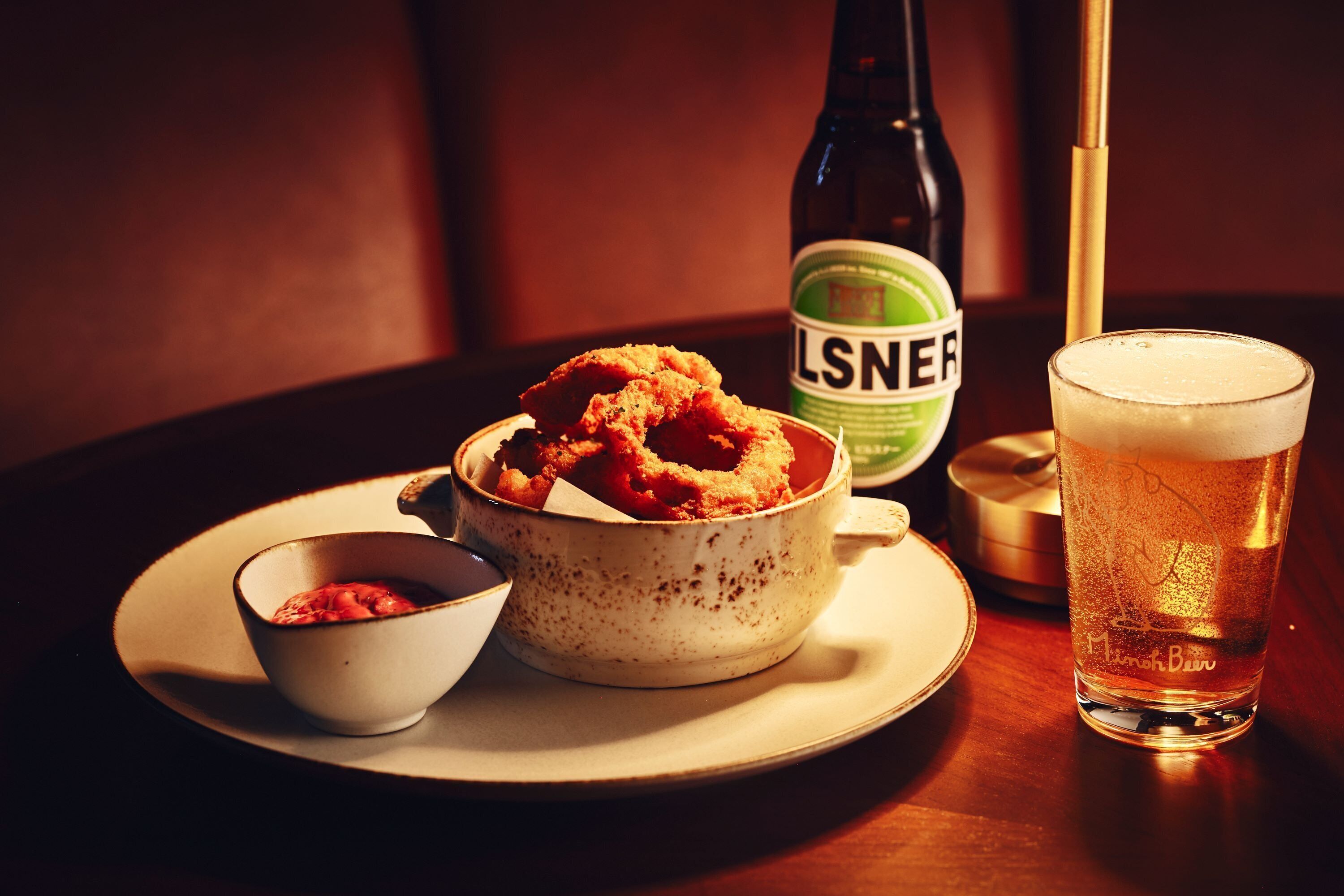 A bowl of fried food, a beer bottle, and a glass of beer on a table.