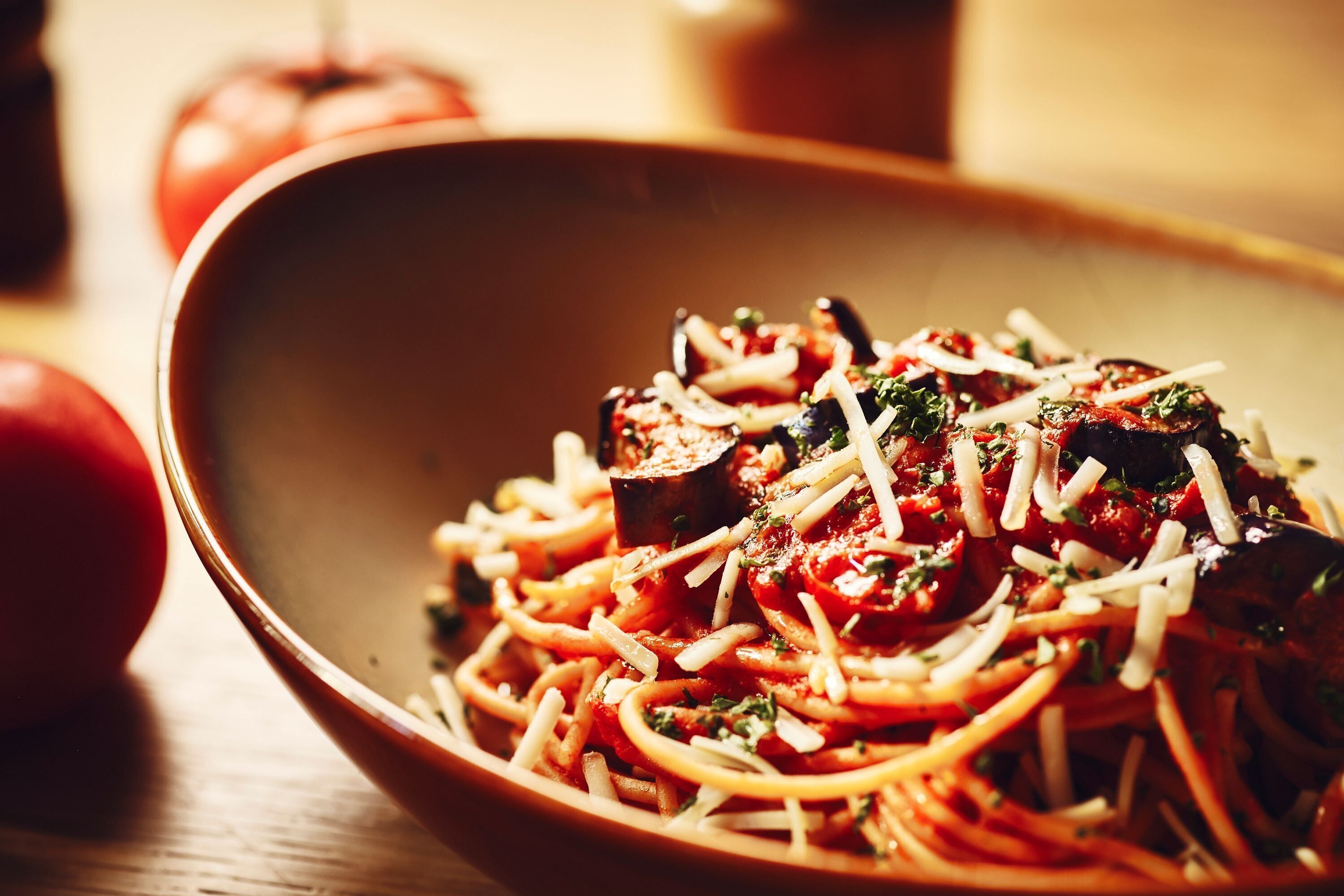 A bowl of spaghetti with tomato sauce and cheese garnished with herbs.