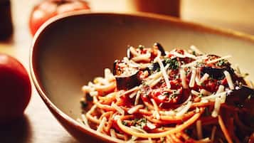 A bowl of spaghetti with tomato sauce and cheese garnished with herbs.