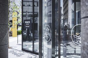 A modern building entrance with glass doors, a sign reading "VOCO", and a reflection of the surrounding cityscape. - voco Osaka Central by IHG (Osaka)
