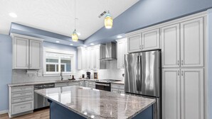 A modern kitchen with white cabinets, stainless steel appliances, and a blue accent wall.