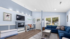 A living room with a blue sofa, a television, a fireplace, and a view of the outside.