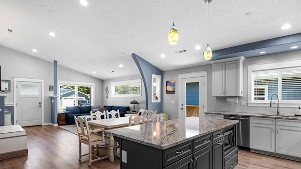 A modern kitchen with a large island, dark cabinetry, and a dining area with a blue sofa.